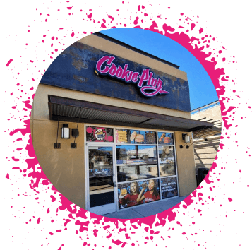 El-Paso-Cookie-Plug-bakery-in-El-Paso-TX Tan and brown storefront with a neon pink, white, and black sign that says 'Cookie Plug' with images of large cookies in the window in assorted flavors.